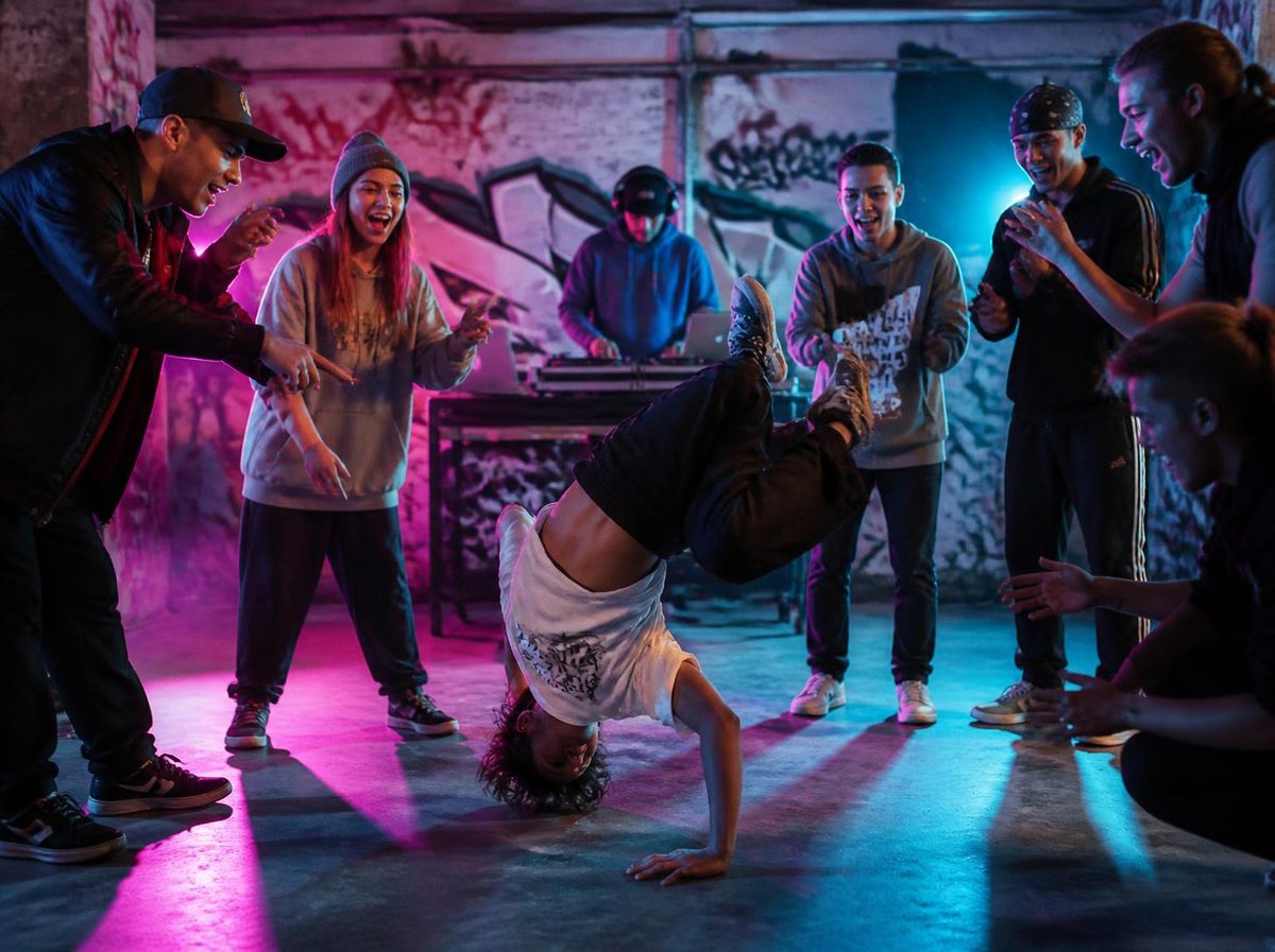 Un breakdancer en figure au sol, encouragé par un cercle de jeunes